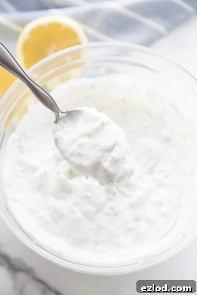 Spoonful of homemade tzatziki dressing above a glass bowl filled with the dressing ready to top Easy Falafel Bites