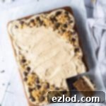 Vegan coffee and walnut traybake cake with a slice cut out on a sheet of baking parchment on a wire rack with chocolate coffee beans and chopped walnuts.