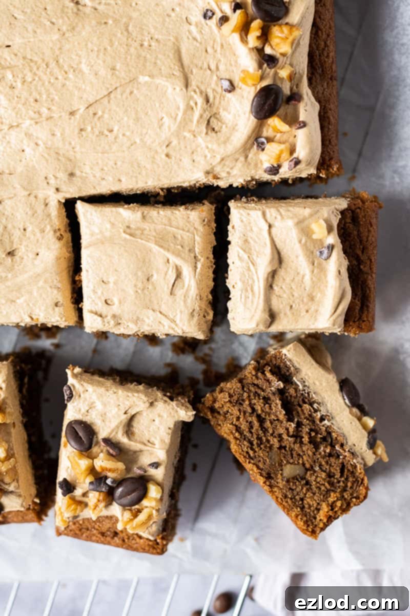 A close-up view of several perfectly cut squares of vegan coffee and walnut cake. Each square is generously topped with a swirl of light and airy coffee buttercream, showcasing the cake's moist texture and inviting decoration. This plant-based traybake is ready for serving a crowd.