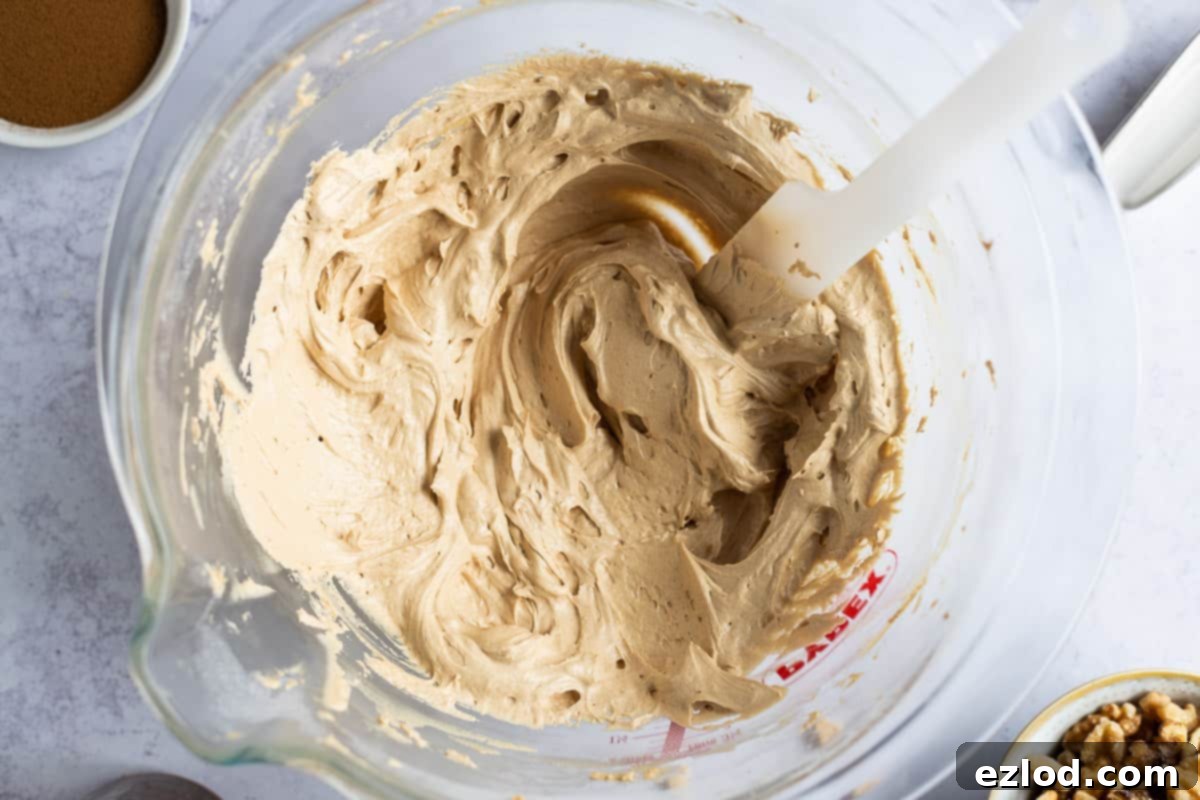 Step-by-step image depicting the creation of coffee buttercream. Softened vegan butter and vegetable shortening are combined with espresso paste, sifted icing sugar, and vanilla extract, being vigorously whisked to achieve a light and fluffy consistency.
