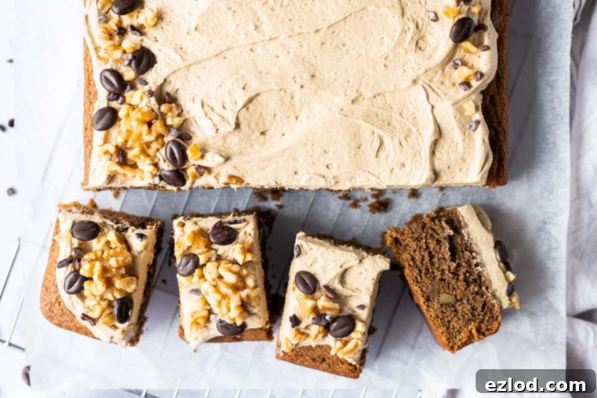 Several neatly cut squares of vegan coffee and walnut traybake cake are arranged on a sheet of baking parchment, emphasizing the convenience and shareability of this easy plant-based dessert. The moist texture is visible, and the portions are ready for serving.