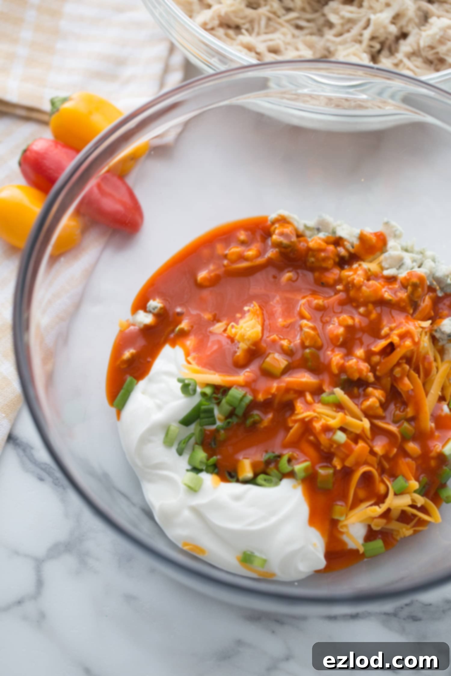 Fiery Buffalo Chicken Stuffed Peppers 6 Overhead photo of a clear glass bowl, filled with the creamy ingredients for Healthy Buffalo Chicken Dip, ready to be mixed with shredded chicken.