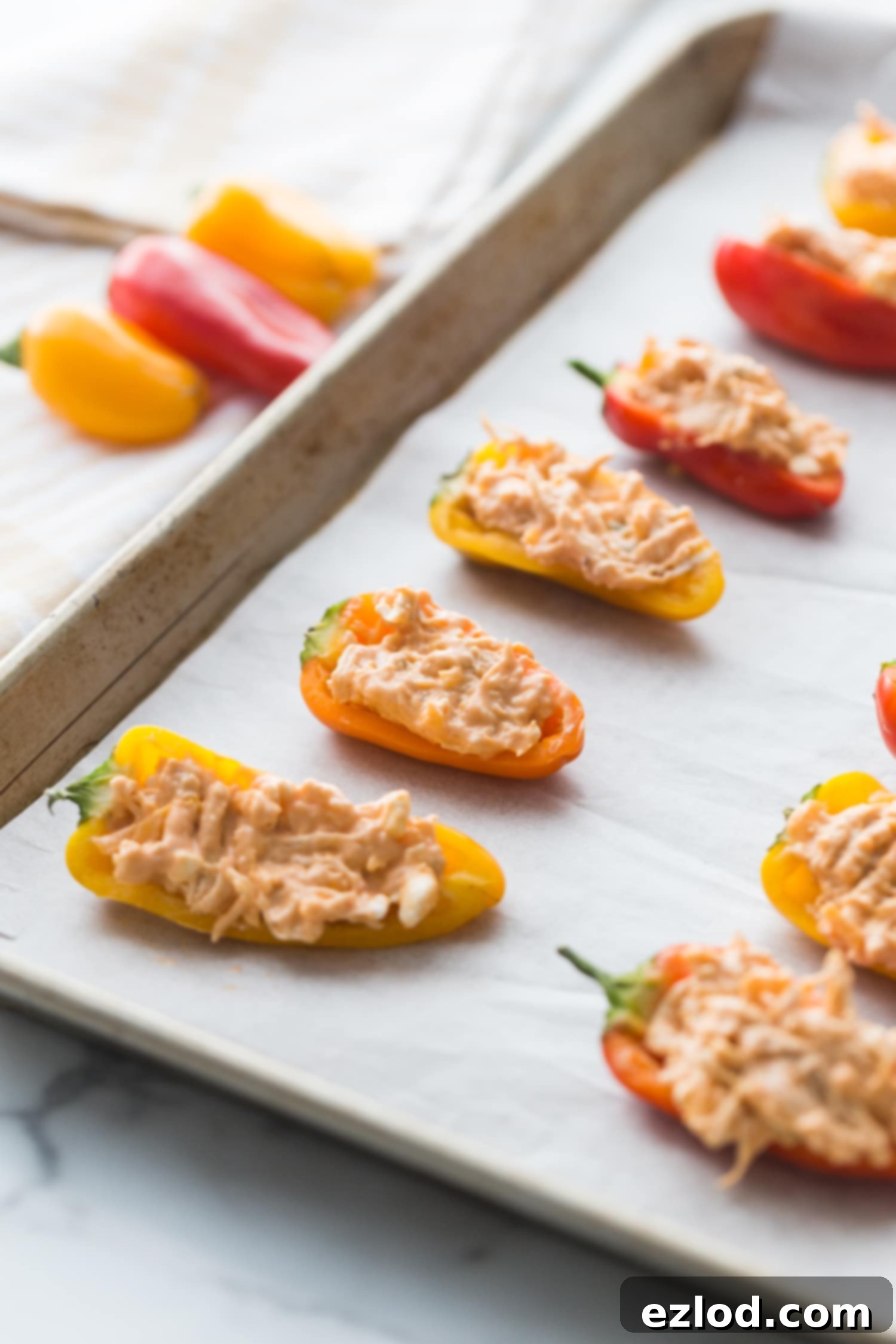 Fiery Buffalo Chicken Stuffed Peppers 10 Close up side angle of a Sheet pan lined with parchment paper with rows of vibrant orange and yellow mini Healthy Buffalo Chicken Dip Stuffed Peppers, showing their cheesy, bubbly topping.