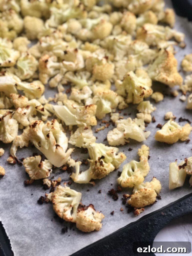 Roasted cauliflower florets seasoned with salt and garlic powder on a parchment-lined baking sheet, ready to be incorporated into Buffalo Cauliflower Dip.