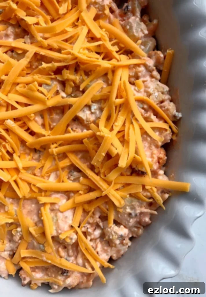 Close-up of unbaked Buffalo Cauliflower Dip in a casserole dish, topped with shredded cheddar cheese, ready to be placed in the oven.