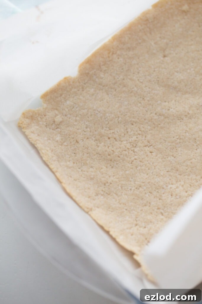 The golden-brown coconut cookie layer of Healthy Samoas Cookie Bars, baked and ready in a parchment-lined pan, awaiting the next delicious layer.