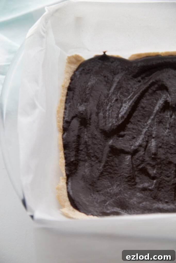 An in-progress photo of Healthy Samoas Cookie bars, showing the smooth, set chocolate layer spread over the coconut cookie base, all within a parchment-lined glass baking dish, chilling in the freezer.
