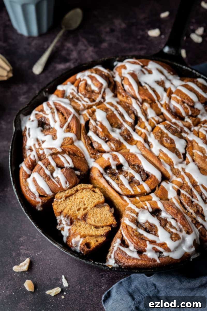 side shot of vegan gingerbread cinnamon rolls in a cast iron skillet, one sliced in half.