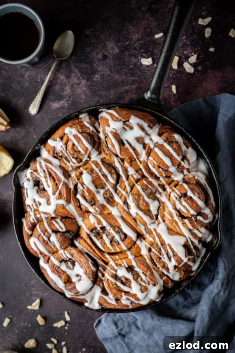 Baked gingerbread cinnamon rolls in a cast iron skillet on a dark background topped with ginger drizzle glaze.