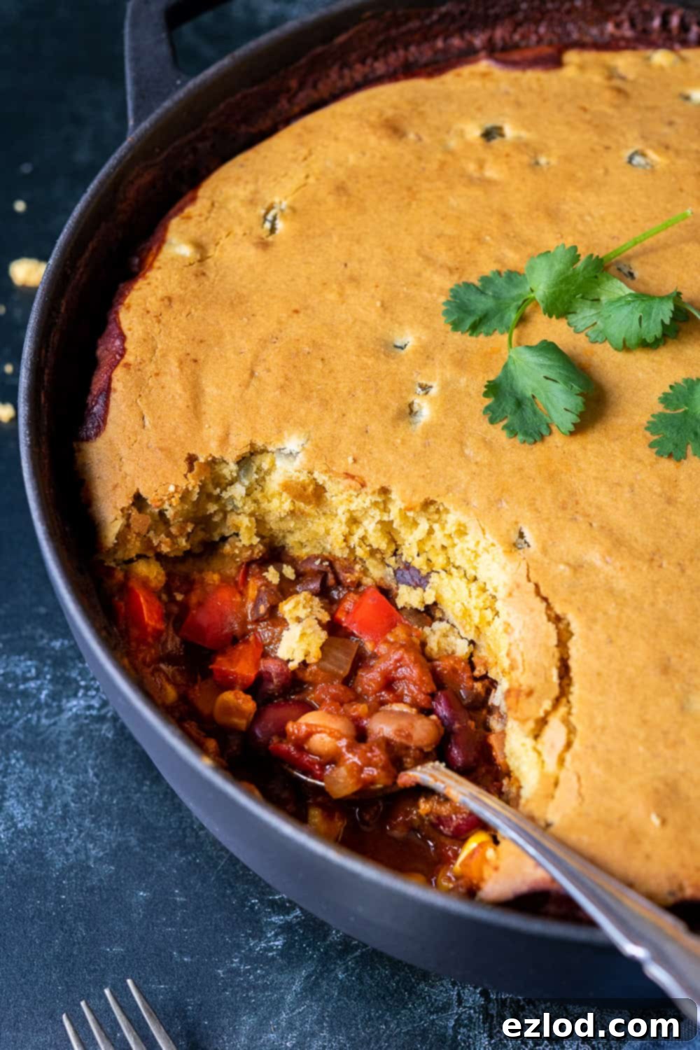 A close-up view of the vegan chili cornbread pie, showing a spoonful already dished out, highlighting the rich chili beneath the golden cornbread.