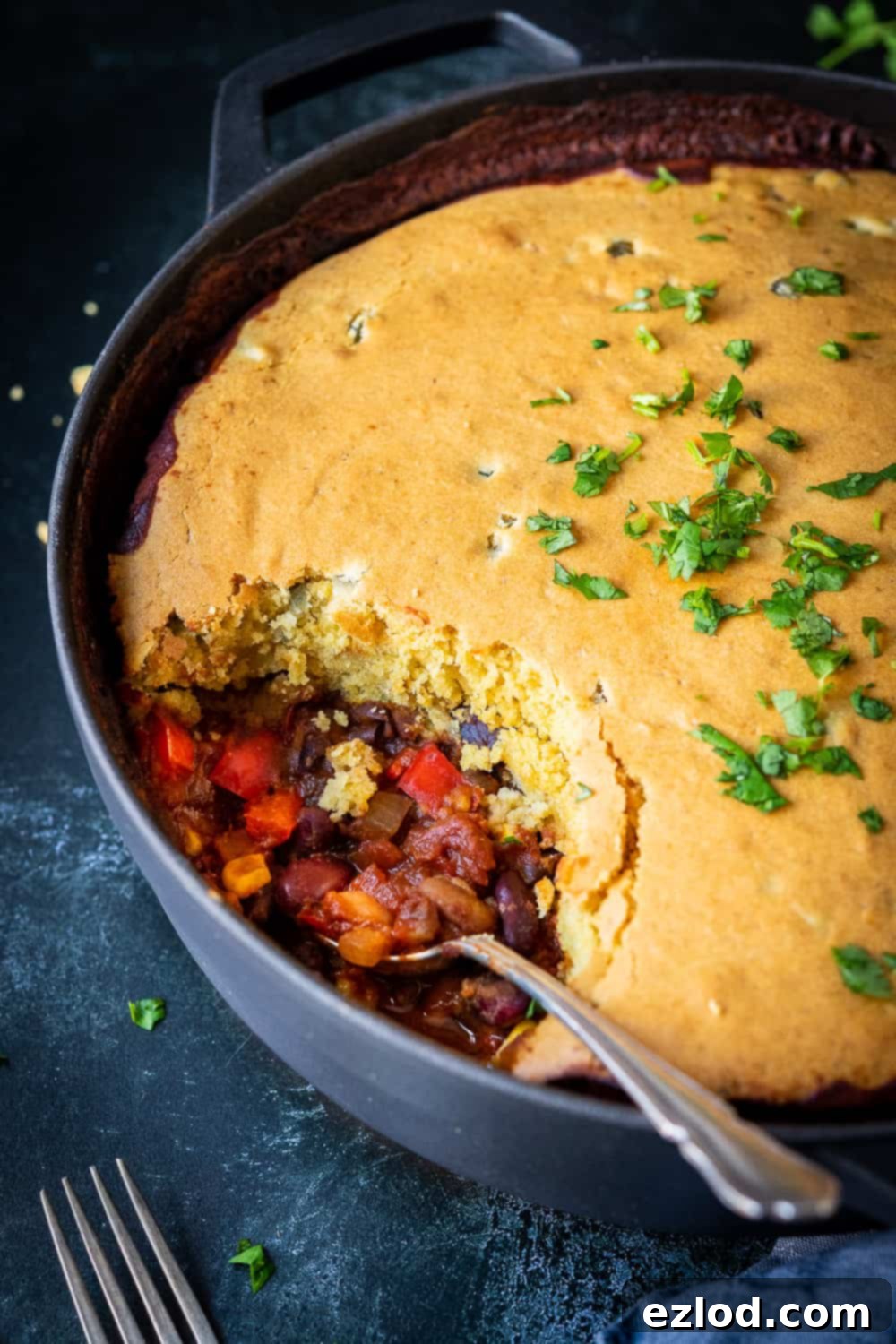 Side view of the vegan chili cornbread pie with a spoonful removed, revealing the layers of chili and cornbread, and a spoon resting in the dish.