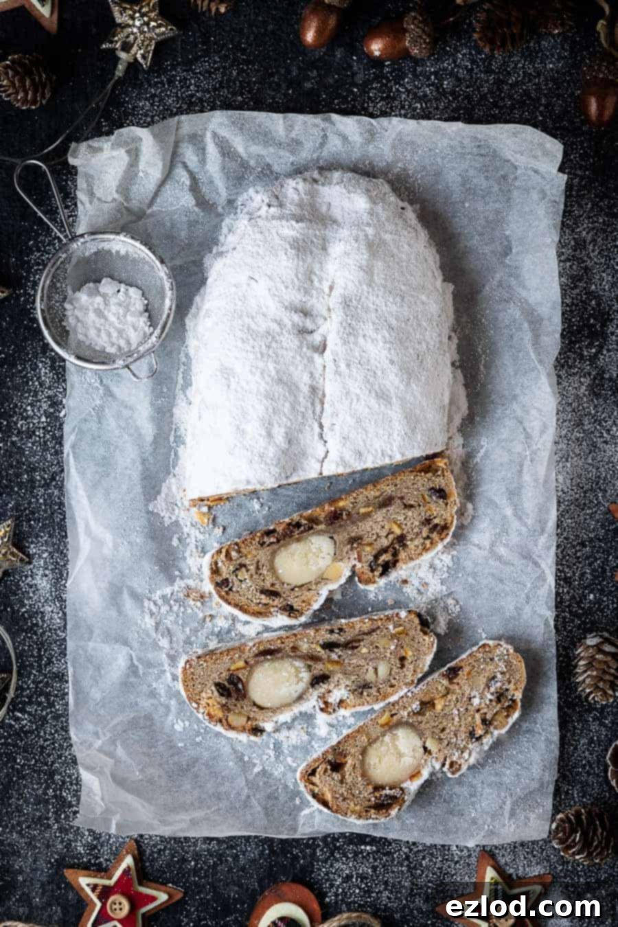 vegan stollen on a sheet of baking parchment on a black surface surrounded by christmas decorations.