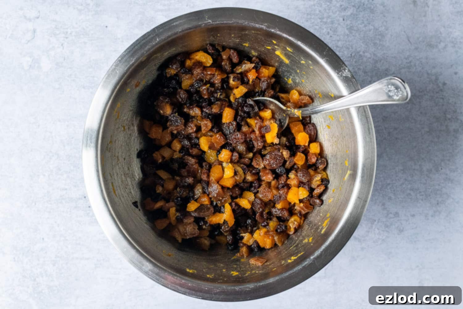 Step-by-step image showing dried fruit (raisins, currants, chopped dates, and apricots) soaking in a bowl with orange zest, orange juice, and rum. This visually explains the first essential step in making vegan Christmas pudding.
