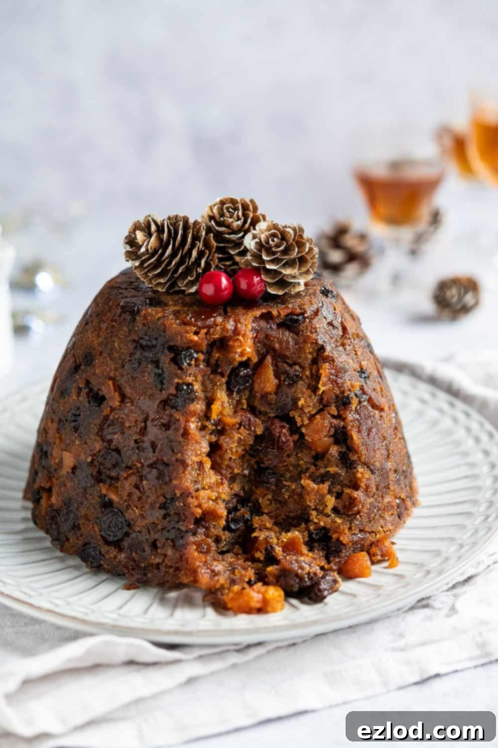 A close-up shot of a vegan Christmas pudding with a spoonful removed, revealing its rich, dark color and the abundance of dried fruits within its moist texture. The focus is on the delicious details of the pudding itself.