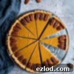 A beautifully baked vegan pumpkin pie, garnished with maple pecans, resting on a metal plate against a soft grey background. Perfect for Thanksgiving and autumnal celebrations.