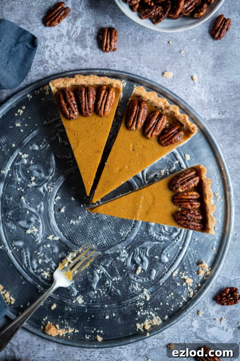 Three perfectly sliced pieces of vegan pumpkin pie, showing the creamy filling and crisp crust, arranged on a metal serving plate.