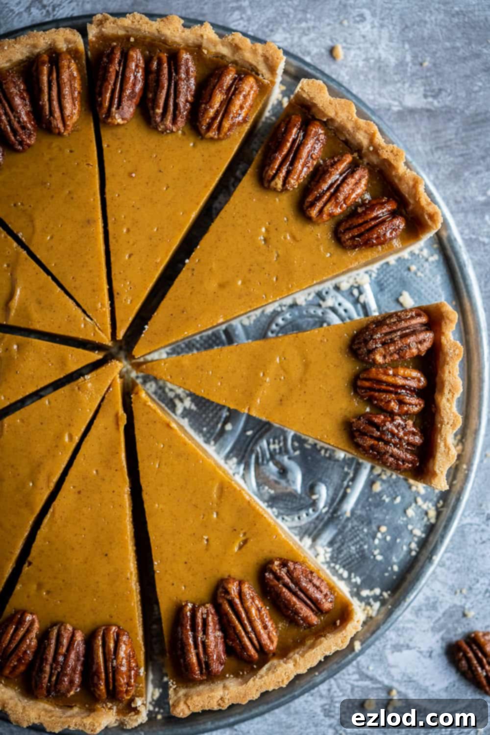 A close-up view of a slice of vegan pumpkin pie, showcasing its smooth filling and garnished with a generous sprinkle of maple pecans on top.