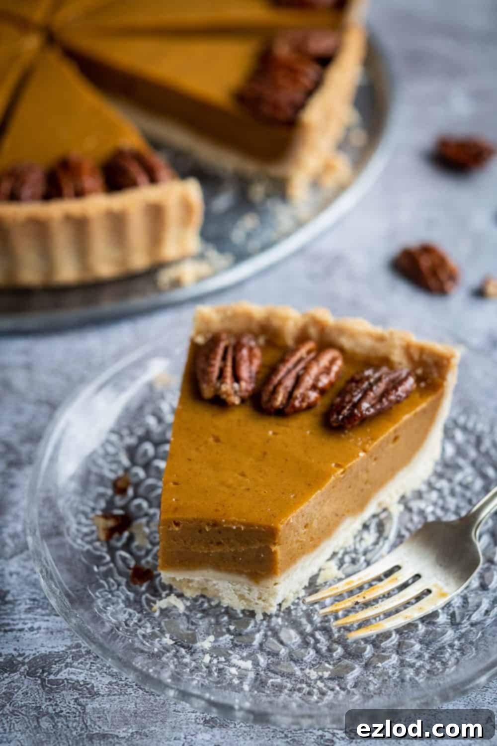 A close-up of a slice of vegan pumpkin pie, with a forkful removed, revealing the creamy texture of the filling and the flaky crust.