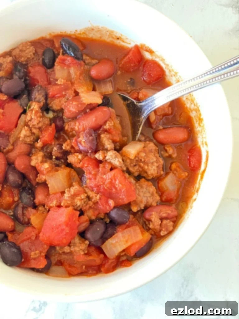 Hearty 5-Ingredient Instant Pot Chili in a white bowl with a spoon, made with pantry staples like beans, diced tomatoes, and onions.