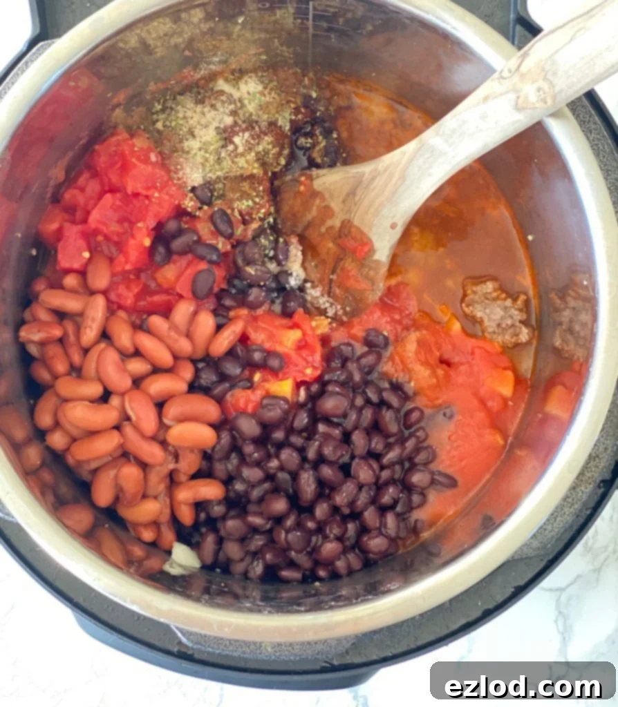 Overhead photo of an Instant Pot with separated ingredients for 5-ingredient chili: black beans, kidney beans, diced tomatoes, tomato sauce, and spices, ready for cooking.