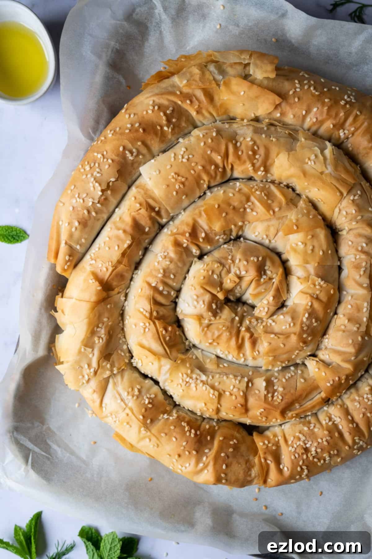 Close-up of baked vegan spanakopita spiral, showing its crispy, golden crust and sesame seed topping.
