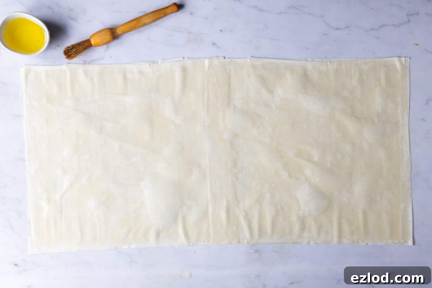 Step-by-step image showing phyllo pastry sheets being layered and brushed with olive oil on a work surface.