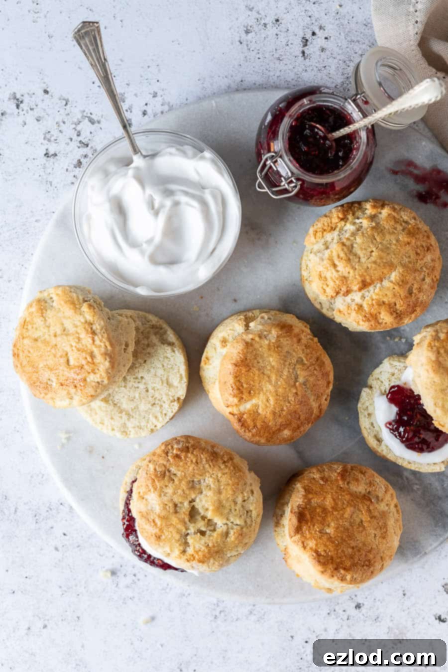 vegan scones on a round marble platter with jam and cream, one sliced in half.