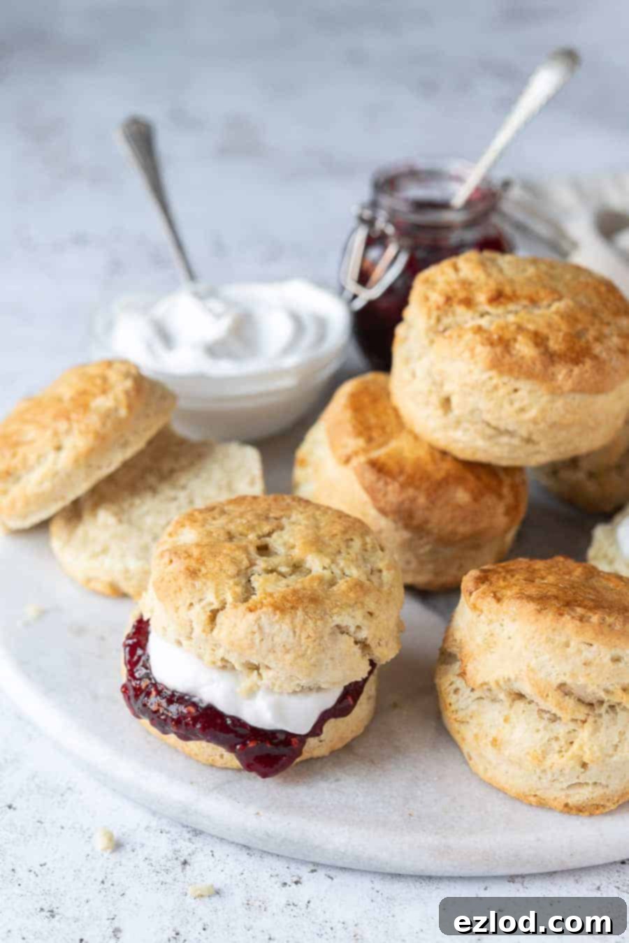 A pile of vegan scones on a marble plate, one filled with jam and cream and one sliced in half.