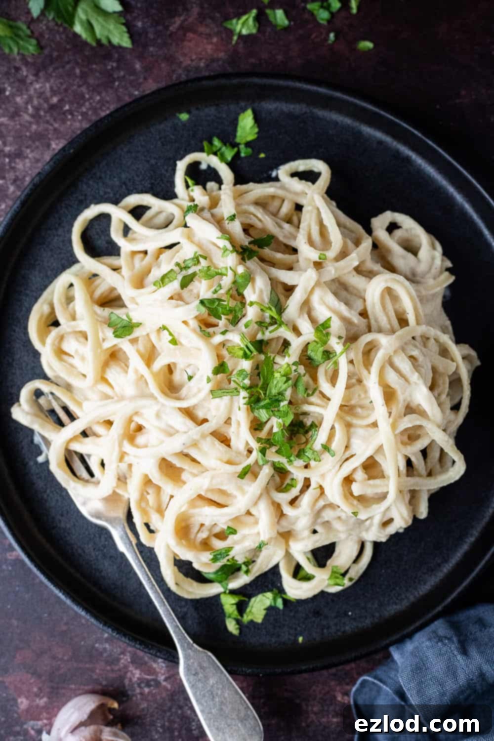 Close up view of creamy vegan cauliflower alfredo pasta on a sleek black plate, ready to be enjoyed.