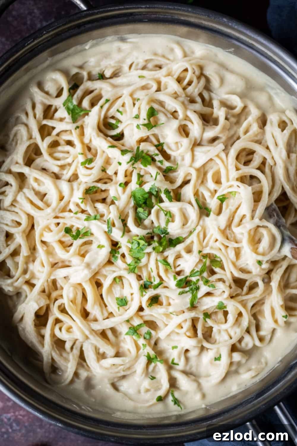 Close up shot of creamy vegan cauliflower linguine in a large metal pan, highlighting the rich texture of the sauce.