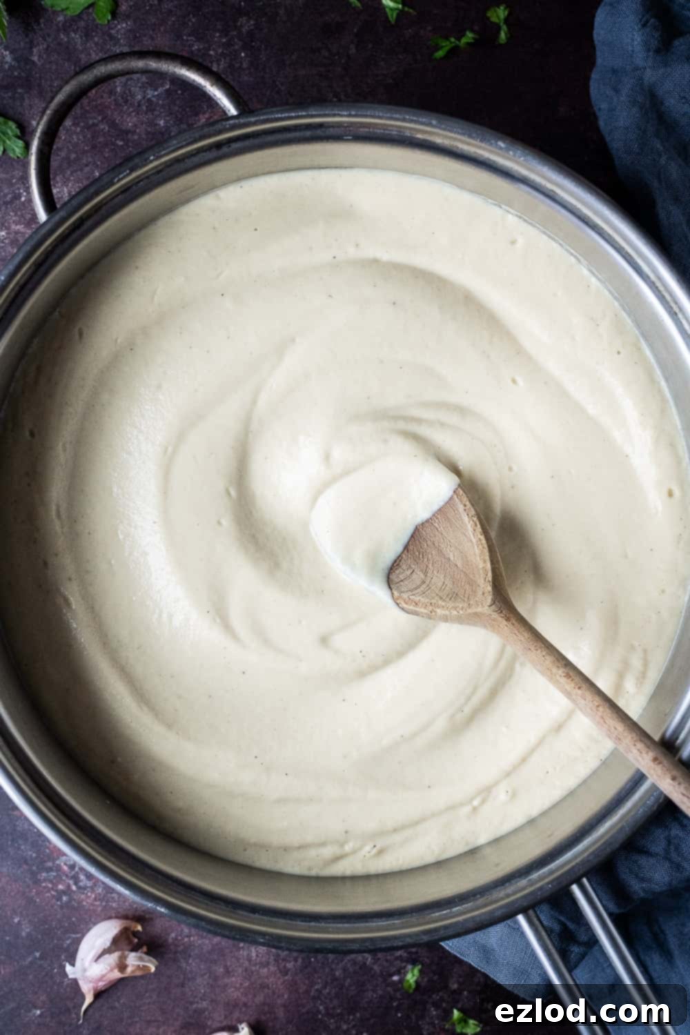 Creamy vegan cauliflower Alfredo sauce in a pan with a wooden spoon, ready to be mixed with pasta.
