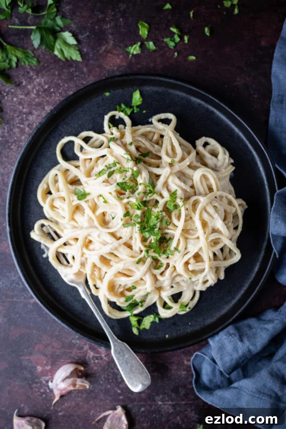 Cauliflower Alfredo linguine served on a black plate with a fork and sprinkled with chopped parsley, set against a dark brown background.
