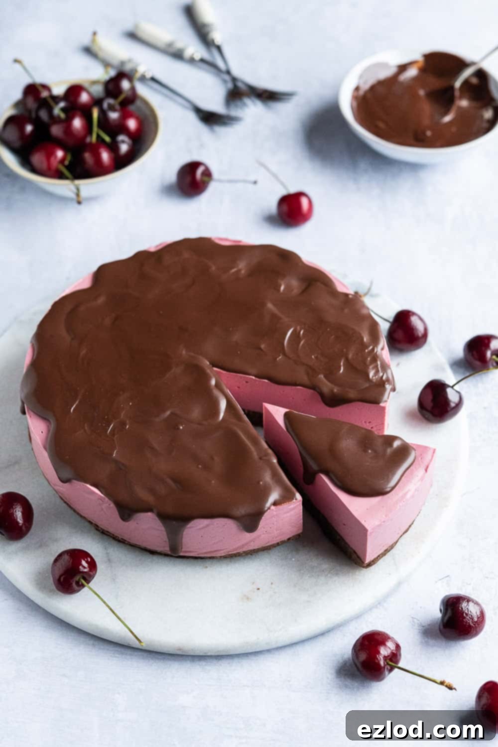 A stunning no-bake vegan chocolate cherry cheesecake with a smooth chocolate ganache and fresh cherries, displayed on an elegant marble platter.