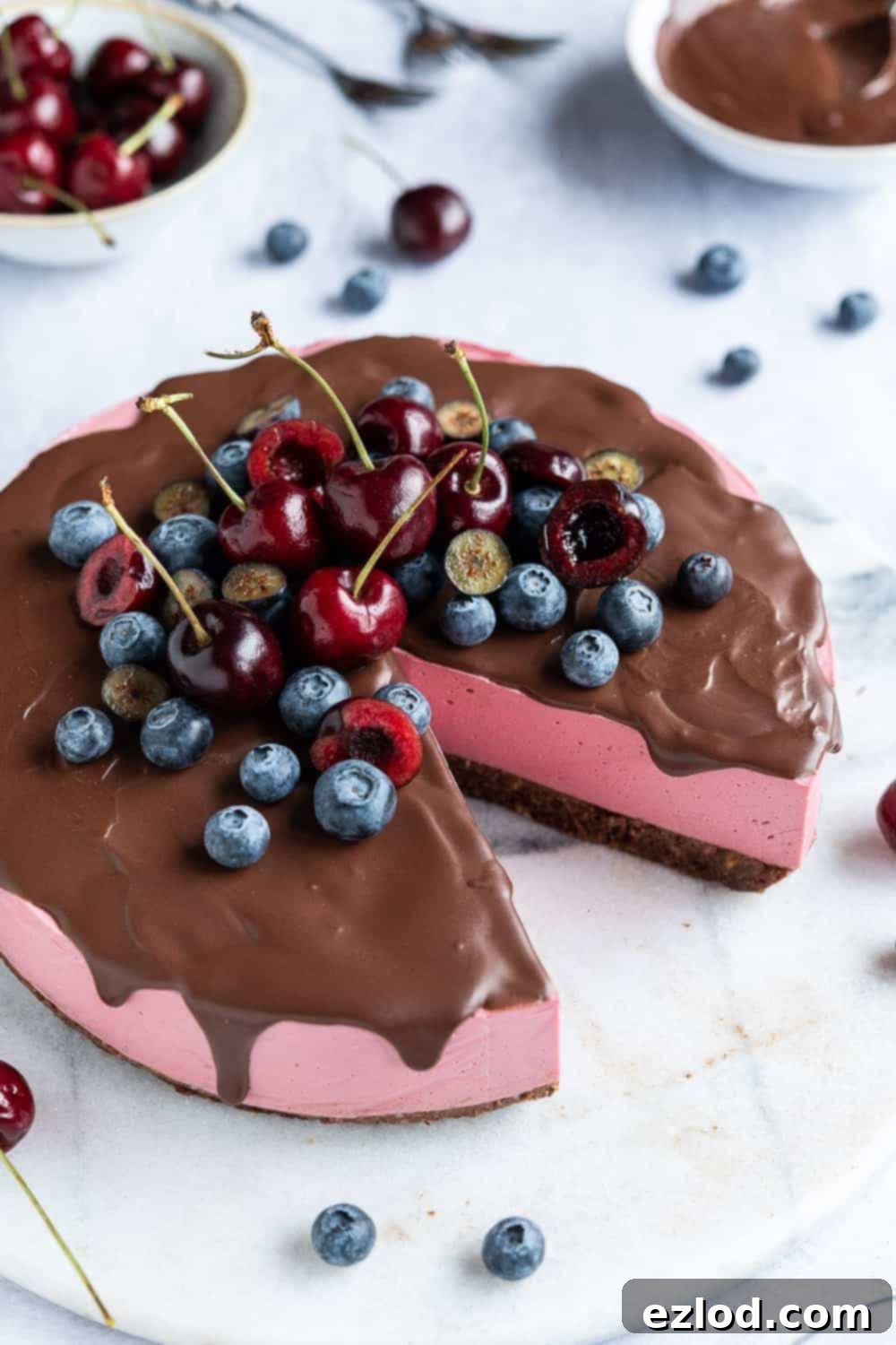The full no-bake vegan chocolate cherry cheesecake, beautifully decorated with a generous pile of fresh blueberries and cherries on top, ready for serving.