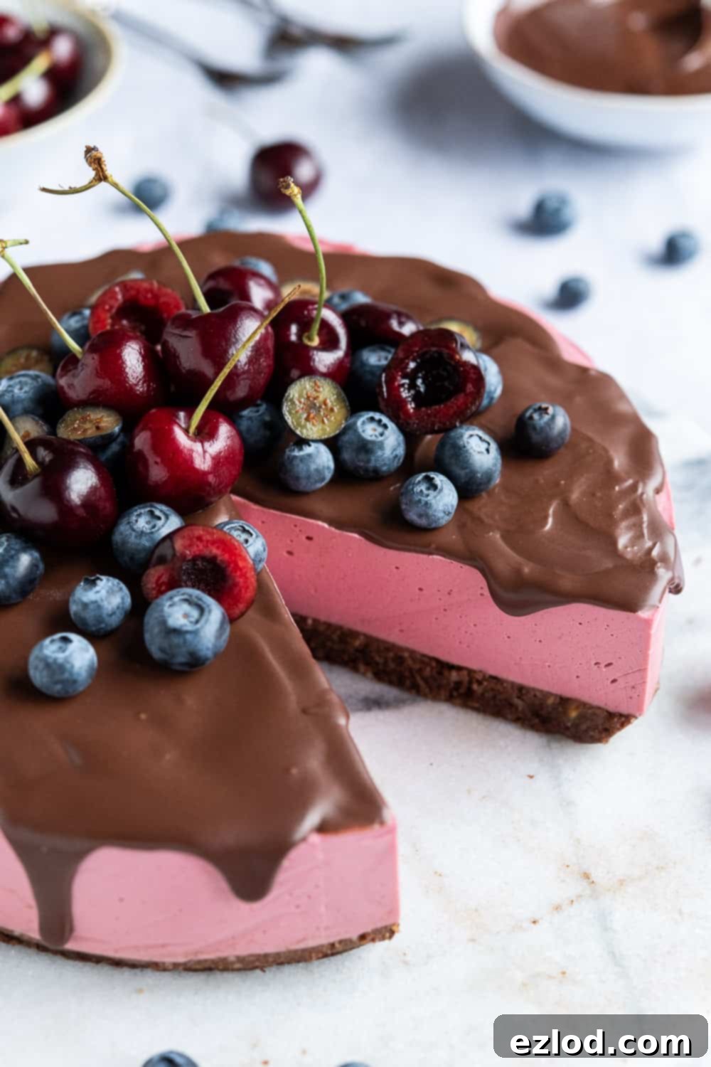 Close up of a whole no-bake vegan chocolate cherry cheesecake, generously topped with an assortment of fresh berries, highlighting its smooth texture and rich color.
