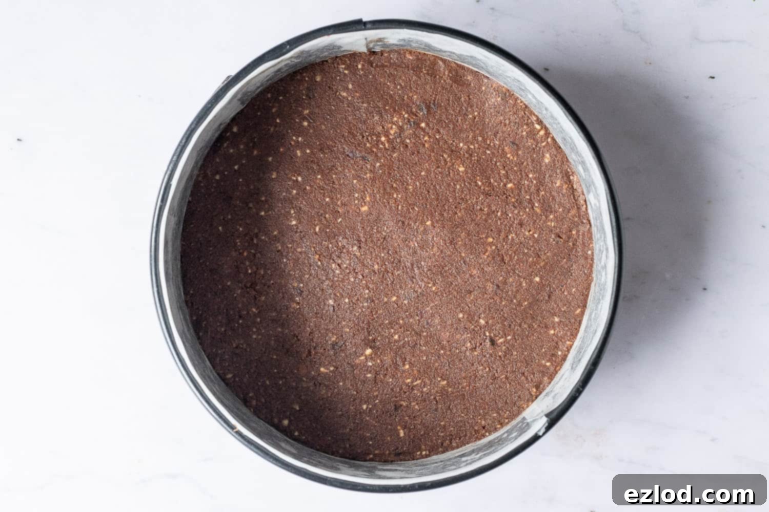 Step 3: The no-bake vegan chocolate cherry cheesecake base, made from nuts, dates, and cacao, is firmly pressed into a lined springform cake tin, ready for the filling.