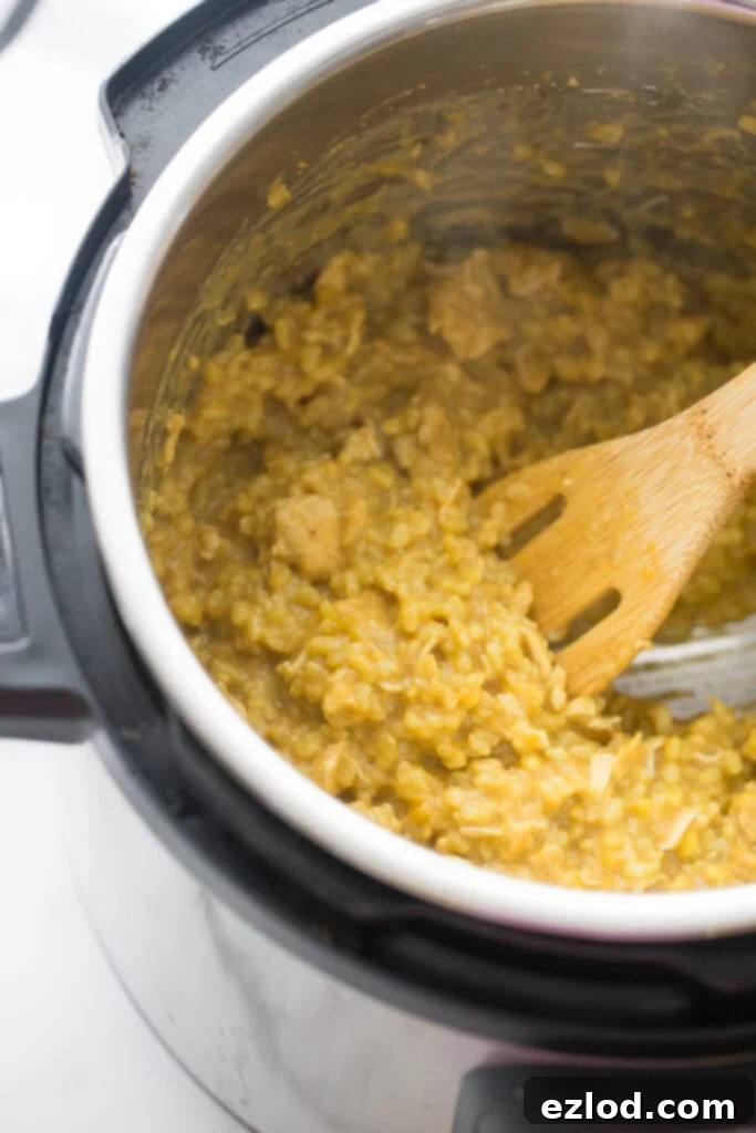 An overhead shot showcasing a wooden slotted utensil gently stirring the rich, cooked Instant Pot Chicken Curry with Rice, highlighting its creamy consistency and vibrant colors.