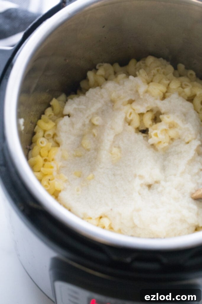 Offset overhead view of an instant pot with cooked gluten free elbow noodles, topped with cauliflower puree, ready to be mixed.
