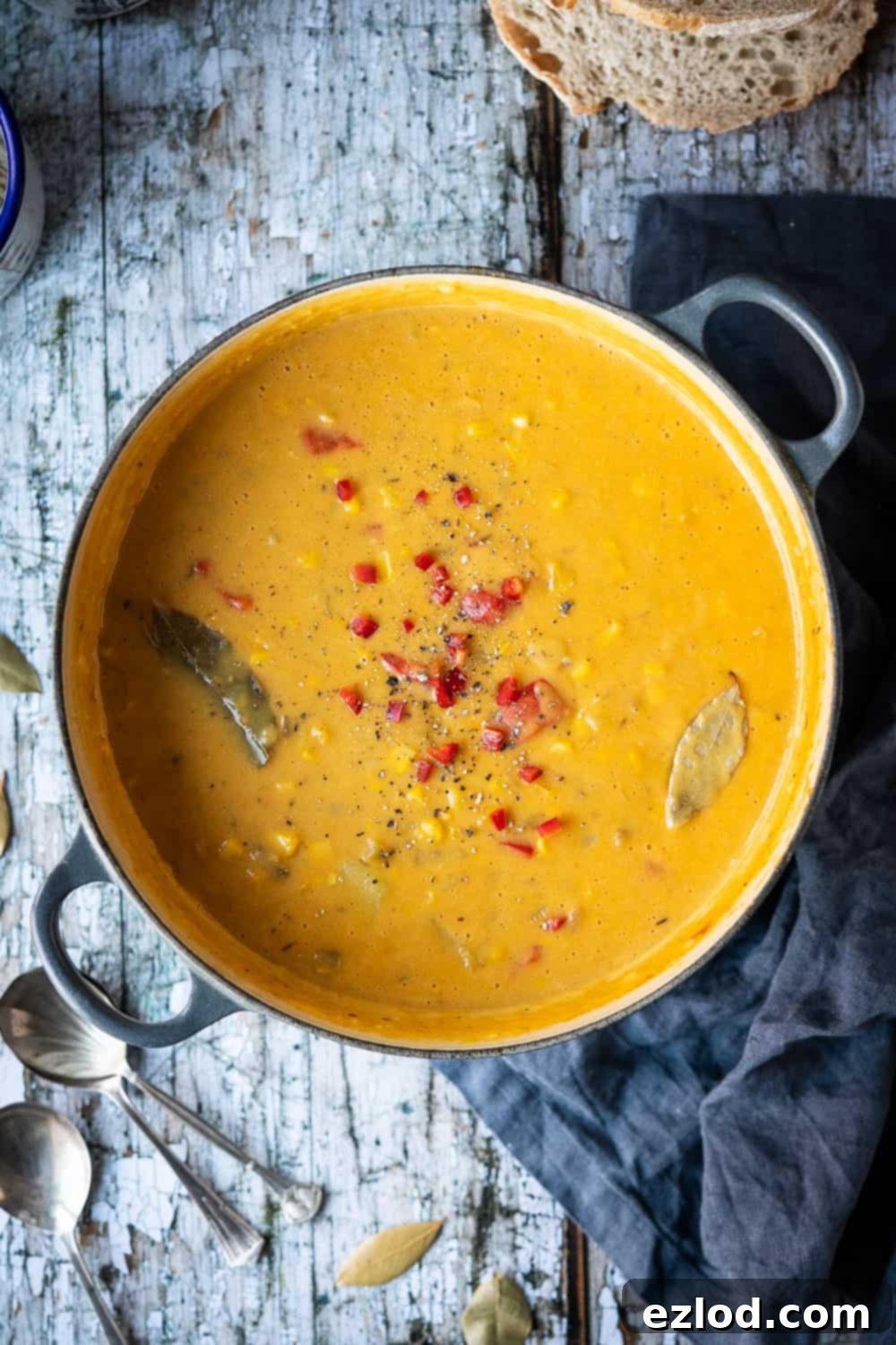 A cast iron panful of vegan corn chowder topped with chopped red chilli on a rustic wood background.