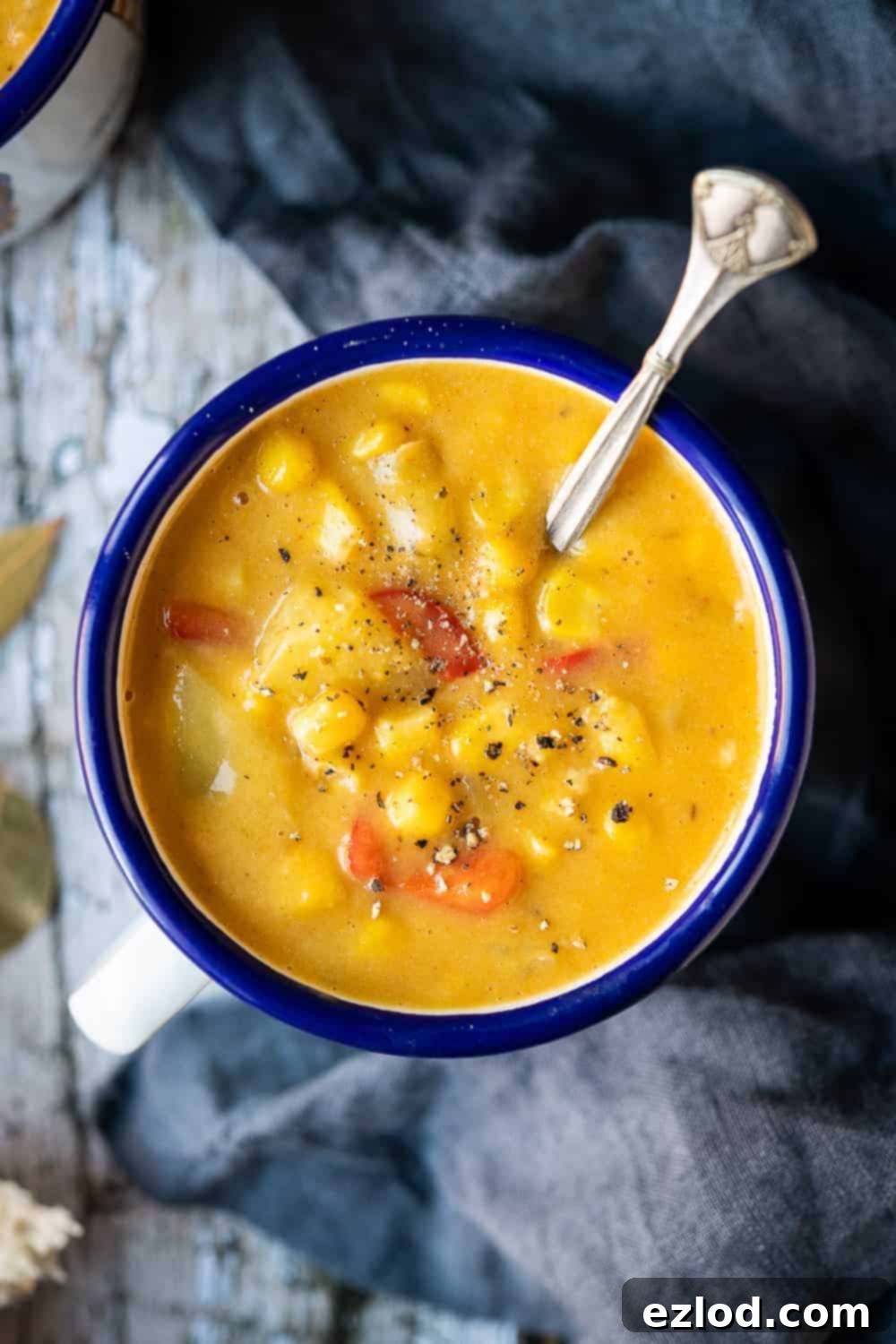 Close up of a blue and white enamel mug of vegan corn chowder on a rustic wood background.