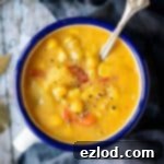 Close up of a blue and white enamel mug of vegan corn chowder on a rustic wood background.