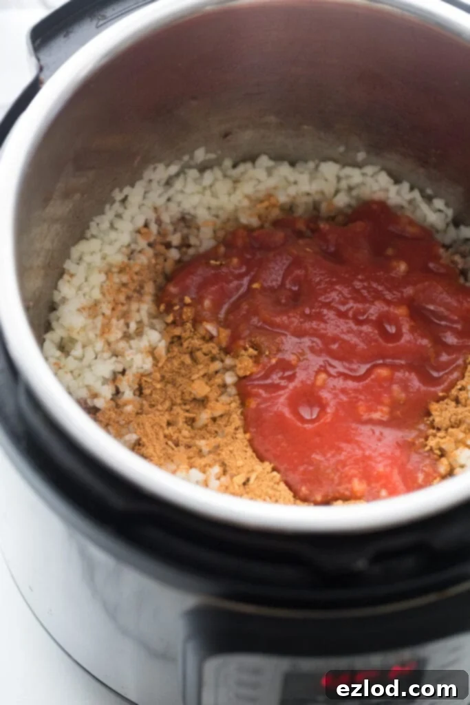 High angle photo of an instant pot filled with cooked beef, cauliflower rice, and tomato sauce, making the filling for beef taquitos.