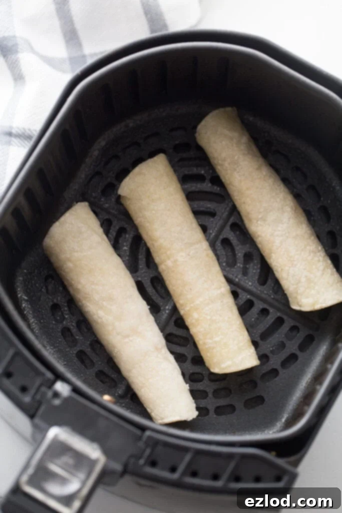 Three beef taquitos in an air fryer basket, ready to be cooked