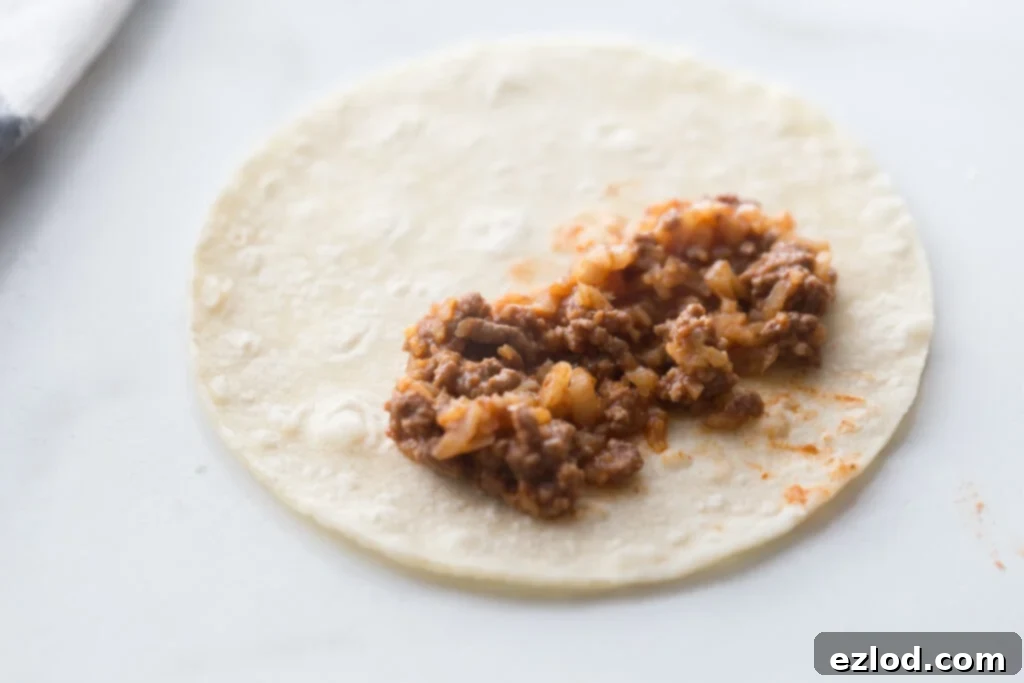 A corn tortilla filled with cauliflower beef taquito filling on a white counter top