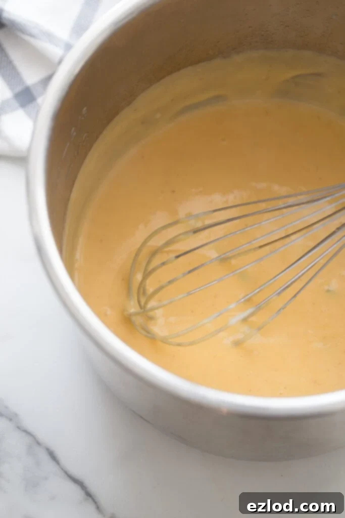 High angle photo of the inner liner of an instant pot with a whisk and finished homemade cheese sauce for beef taquitos.