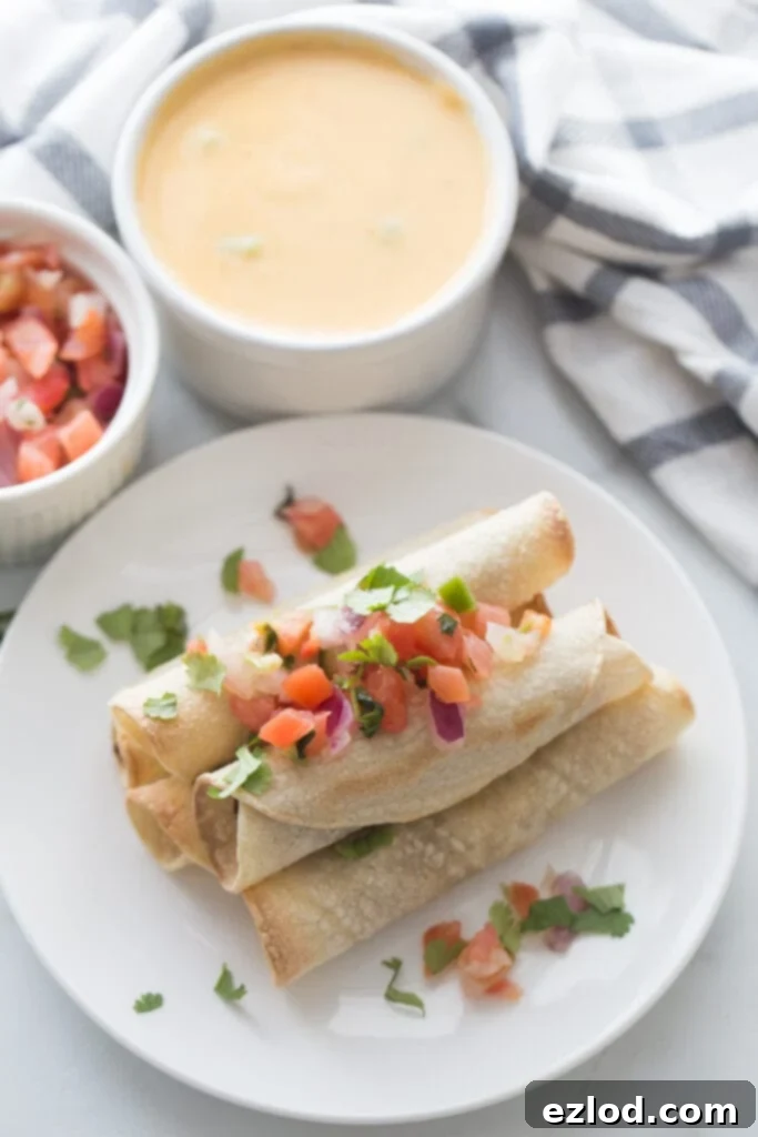 Overhead photo of a plate stacked with beef taquitos topped with homemade salsa. Ramekins filled with salsa and homemade cheese sauce are next to the plate.