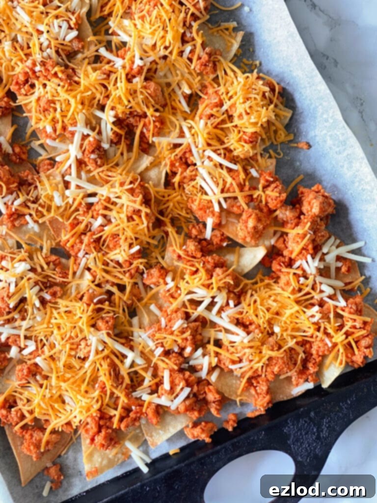 In process sheet pan nachos with the tortilla chip, beef, and cheese layers.