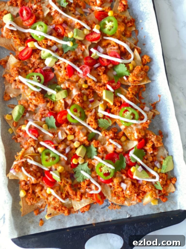 Homemade nachos topped with ground beef, cheese, jalapeno, tomatoes, corn, cilantro, avocado, and drizzled Greek yogurt on a parchment lined sheet pan.