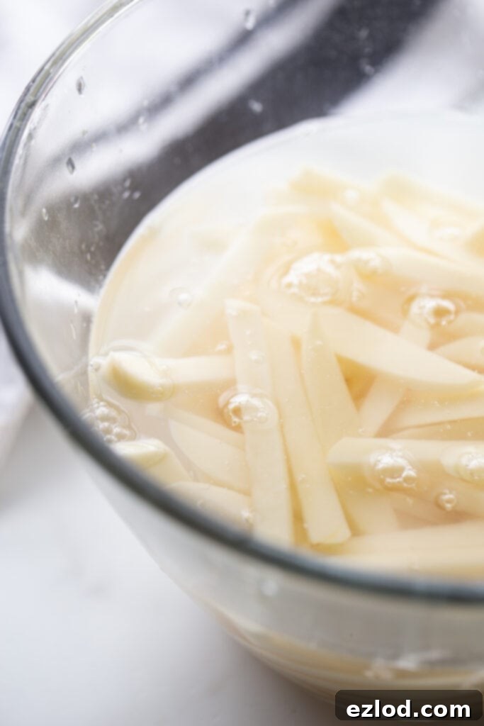 Raw thin cut potatoes soaking in water in a glass bowl. 