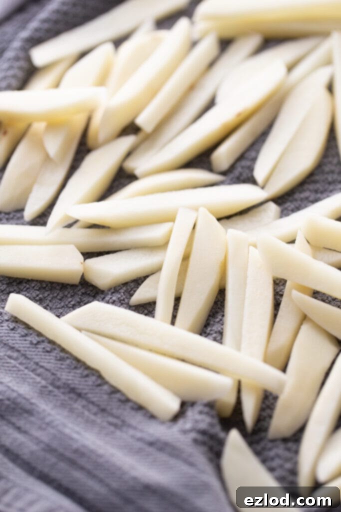 Thin cut raw potatoes drying on a dark gray kitchen towel, ready for the air fryer or oven.